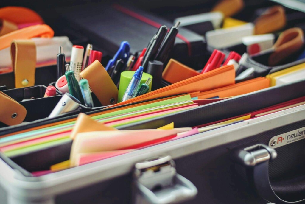 Open briefcase with organized colorful stationery, including pens, markers, notebooks, and folders. The setup conveys organization and productivity.